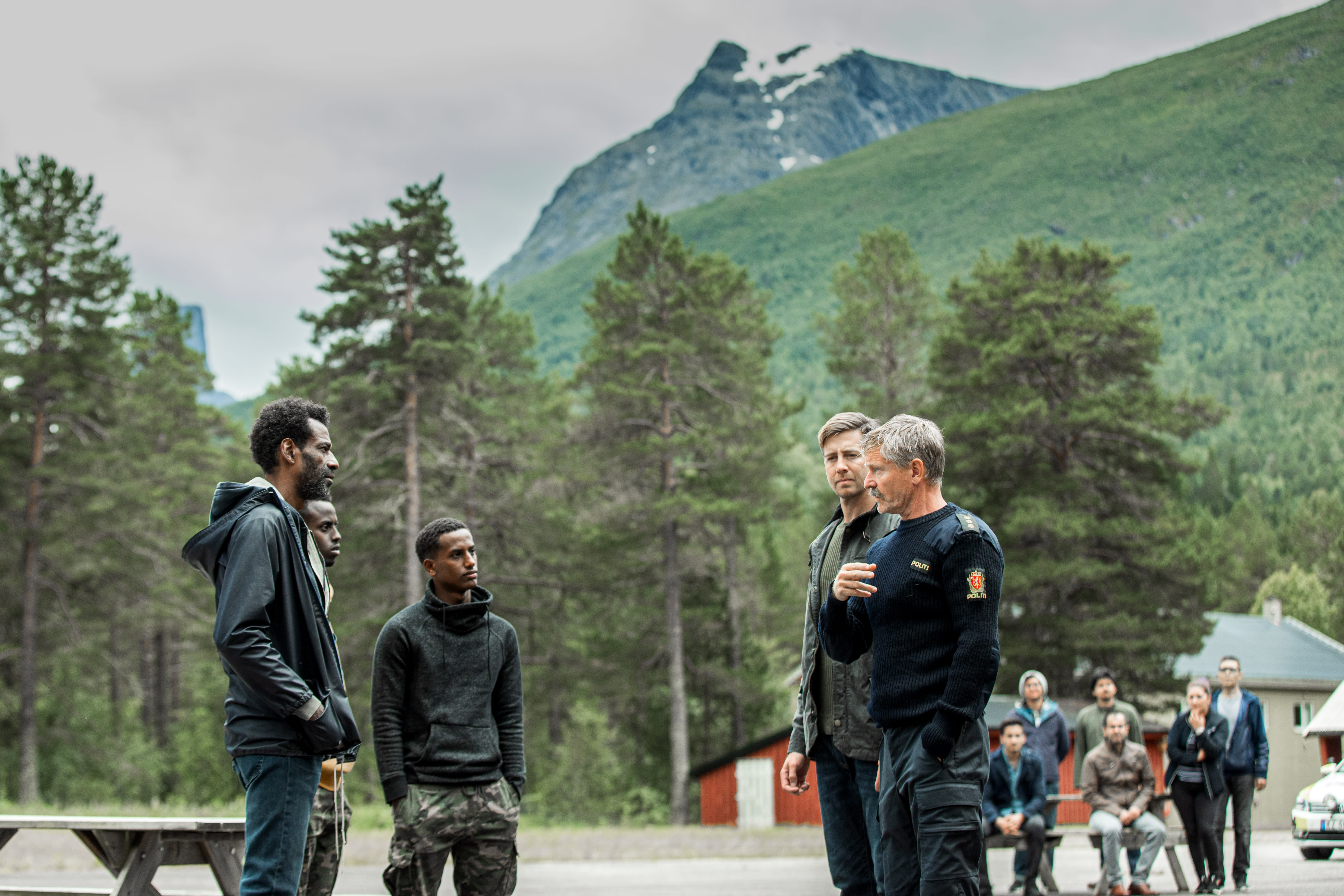Lensmannen (Henrik Mestad) og politimannen Asgeir (Pål Sverre Hagen) avhører flyktninger etter at det er oppdaget hærverk på mottaket. 