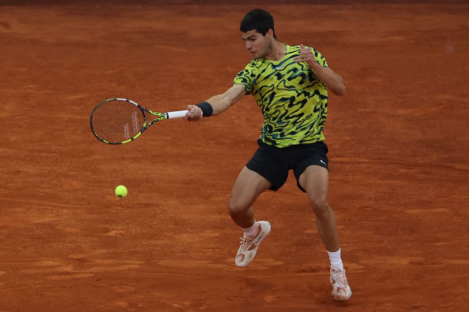 En ung mann med svart hår og selvlysende skjorte slår et slag i tennis.