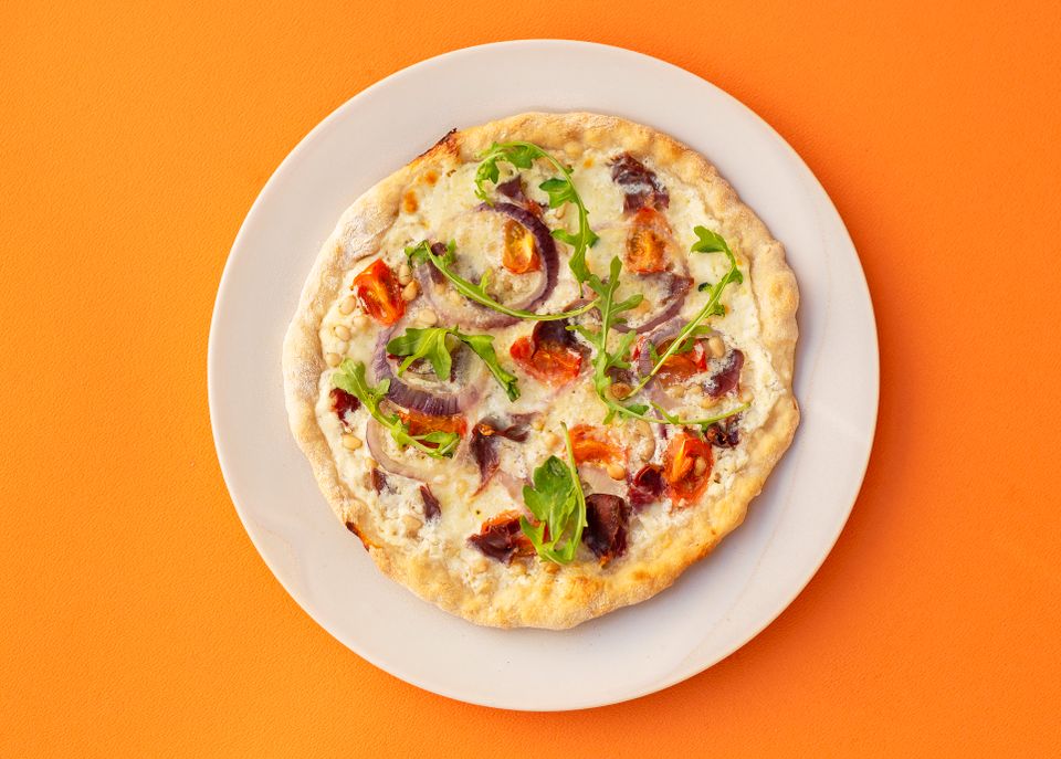 Et hvitt fat med en pizza med hvit saus og ruccola oppå, ligger på en knalloransje bakgrunn.