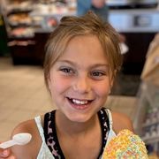 Nærbilde av en jente med brunt hår festet bak hodet som smiler mens hun spiser en is med strøssel på.