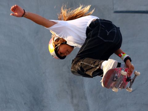 En jente har på seg hjelm og er midt i et triks på skateboard.