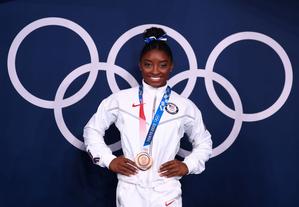 Dame i hvit treningsjakke står på et podium med en medalje rundt halsen