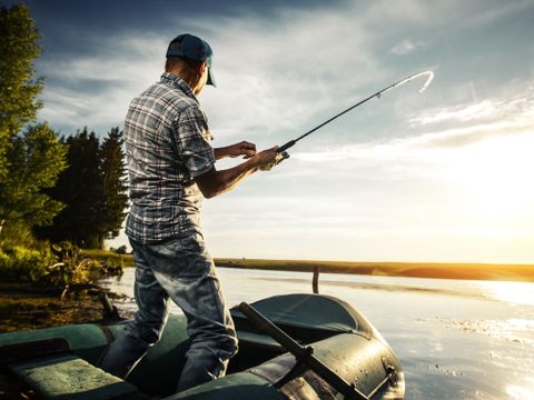 En mann står i solnedgang og fisker med fiskestang.
