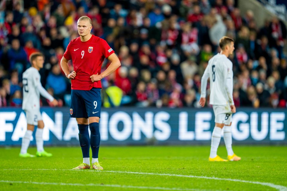 En fotballspiller i rød trøye står skuffet og holder seg på hoftene.