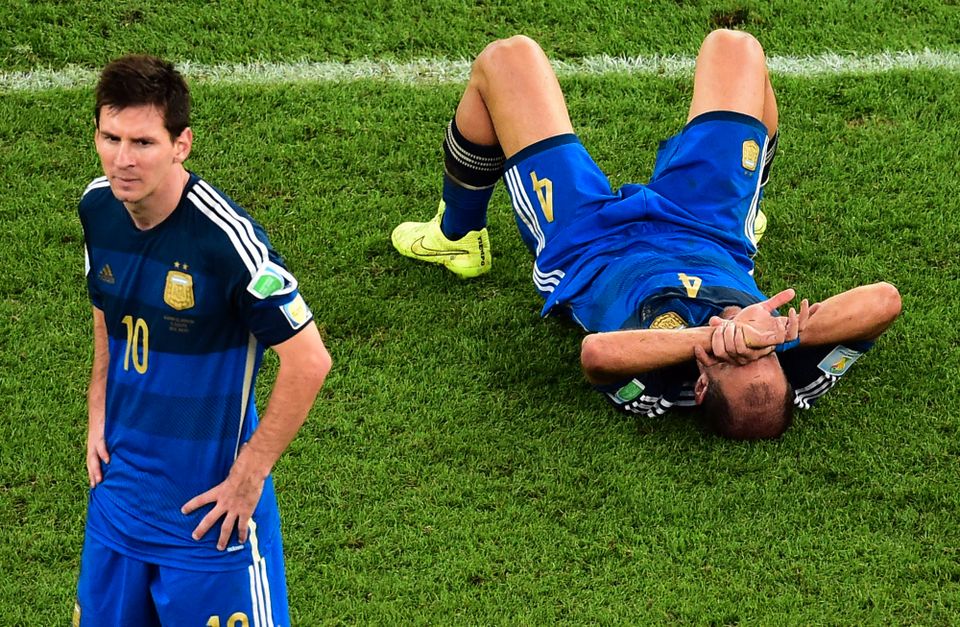 En fotballspiller i blå drakt ser veldig skuffet ut og en lagkamerat ligger på bakken og er lei seg.