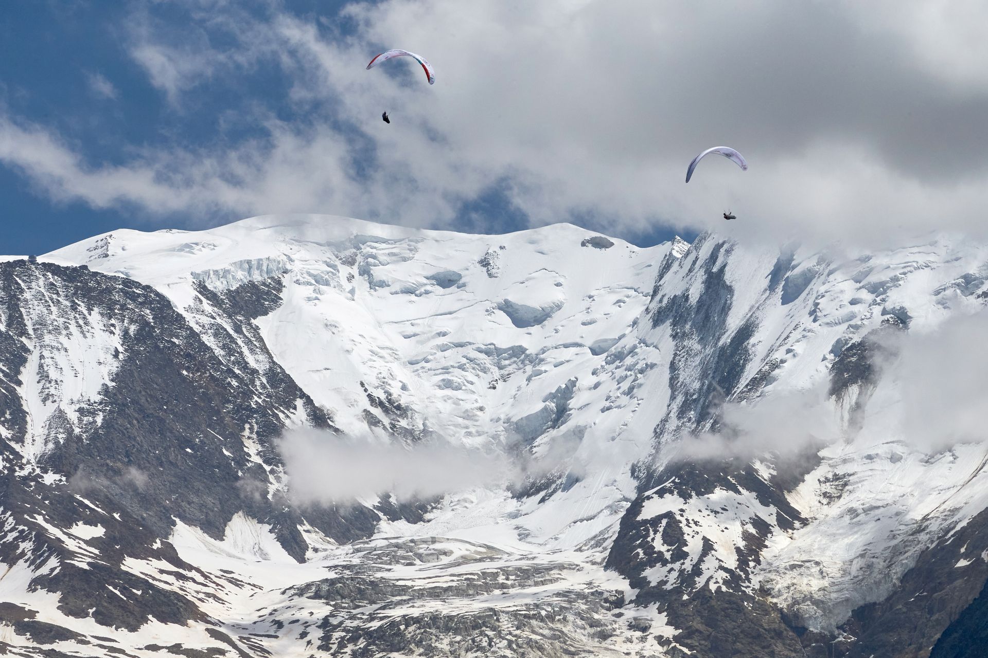 To paraglidere seiler på en blå himmel med isdekkene Mont Blanc i bakgrunnen.