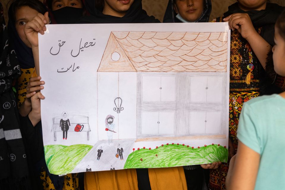 Jentene holder opp en tegning for kameraet.  Tegningen viser en Taliban-soldat som blokkerer inngangen til en skole. På tegningen står det: «Utdanning er vår rettighet.»