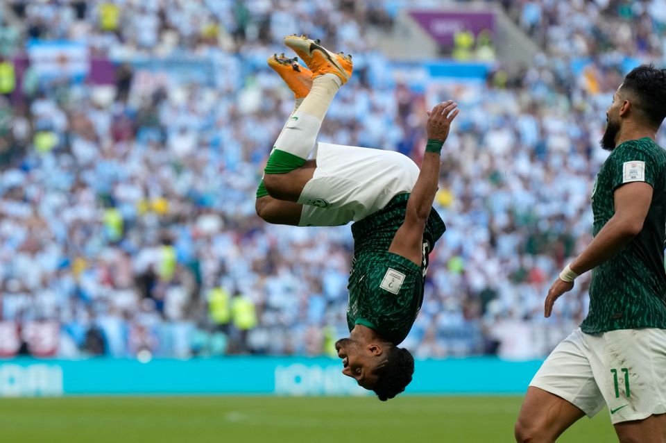 En fotballspiller i grønn drakt er opp ned i luften fordi han tar en salto og feirer et mål.