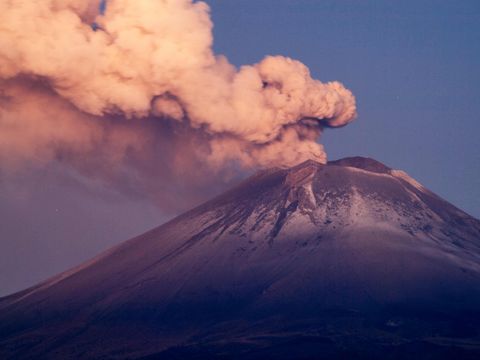 En stor vulkan i halvmørke spyr tykke røykskyer opp i luften.