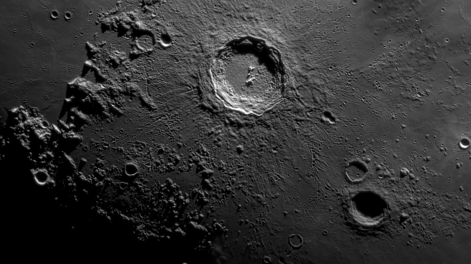 Et nærbilde av Månens overflate viser en støvete, mørkegrå grunn med et stort, rundt krater i. 