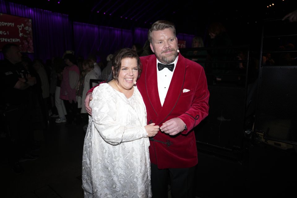 En kvinne i hvit brudekjole og en mann i rød dress holder rundt hverandre og smiler