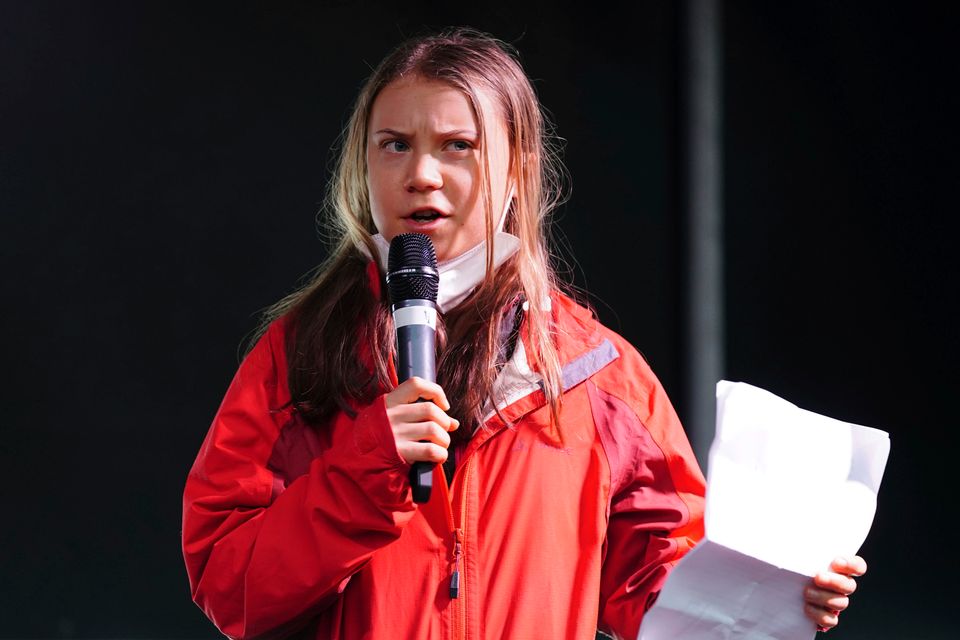 En seriøst ung kvinne i rød jakke holder en mikrofon og holder en tale.