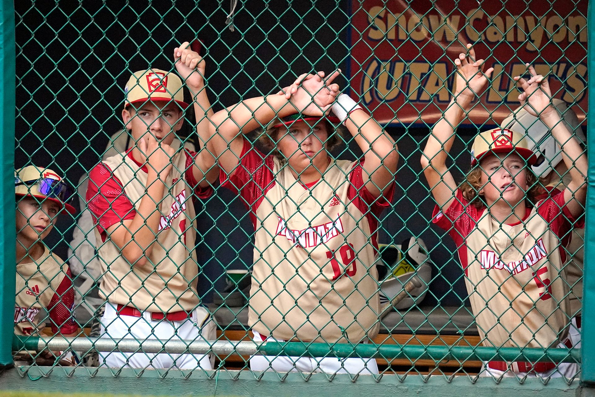 Tre gutter i beige T-skjorte med røde ermer og caps står bak et metallgjerde og henger