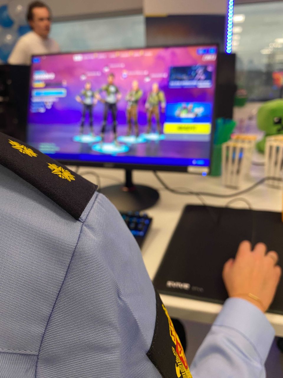 Vi ser armen til en politibetjent i uniform som sitter foran en PC-skjerm som viser spillfigurer.