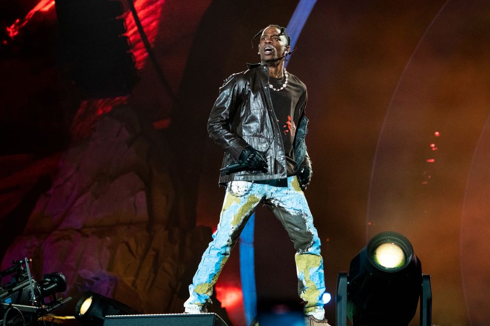 En seriøs rapper står på scenen i sort jakke og olabukse.