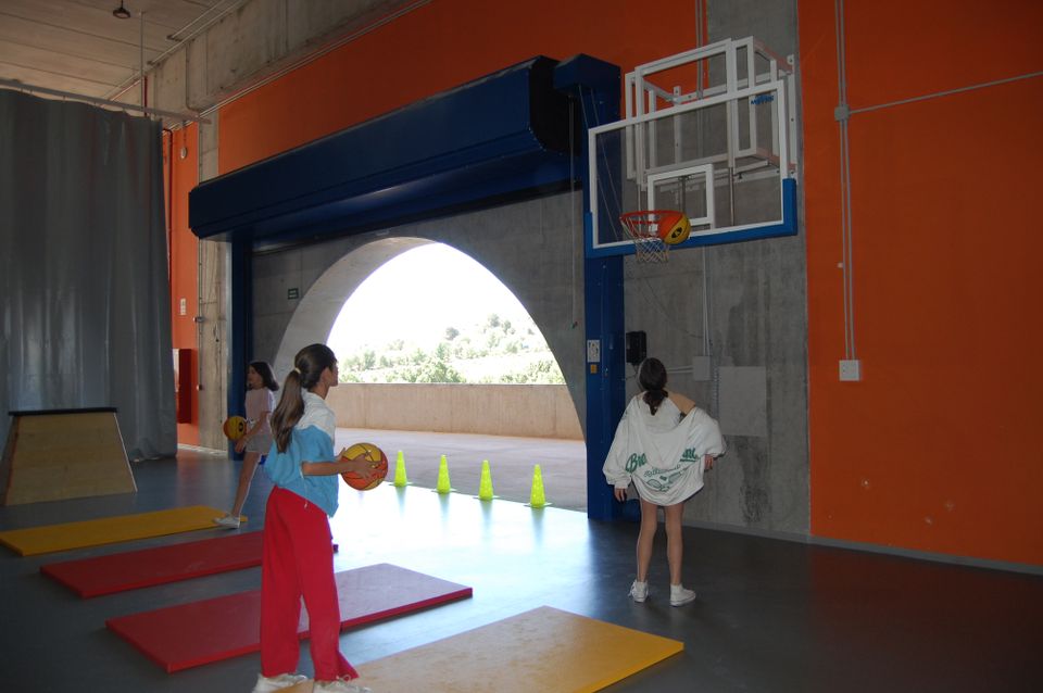 Tre jenter i en stor betonggymsal som spiller basket