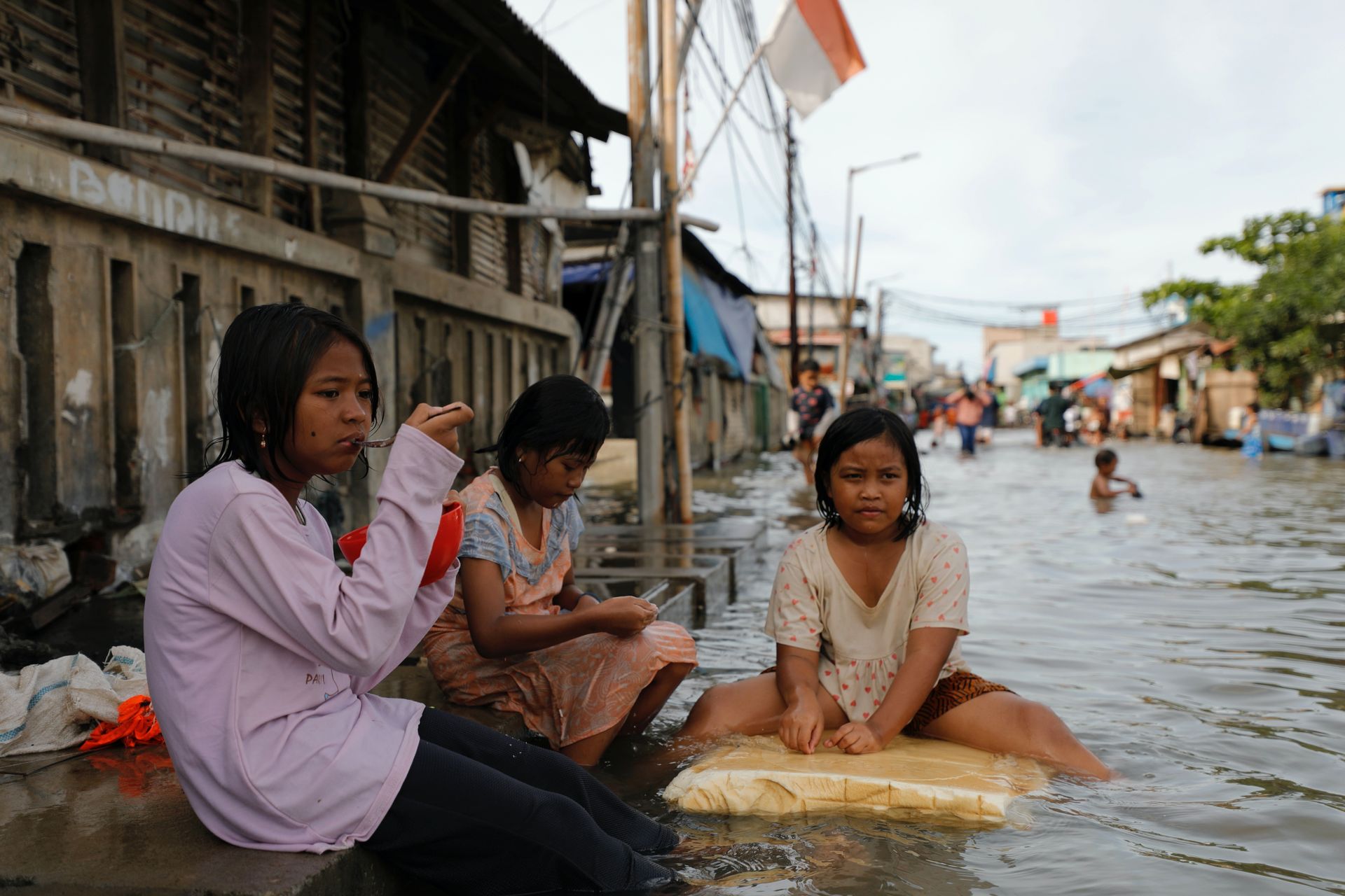Tre unge jenter sitter i en gate som er dekket av vann.