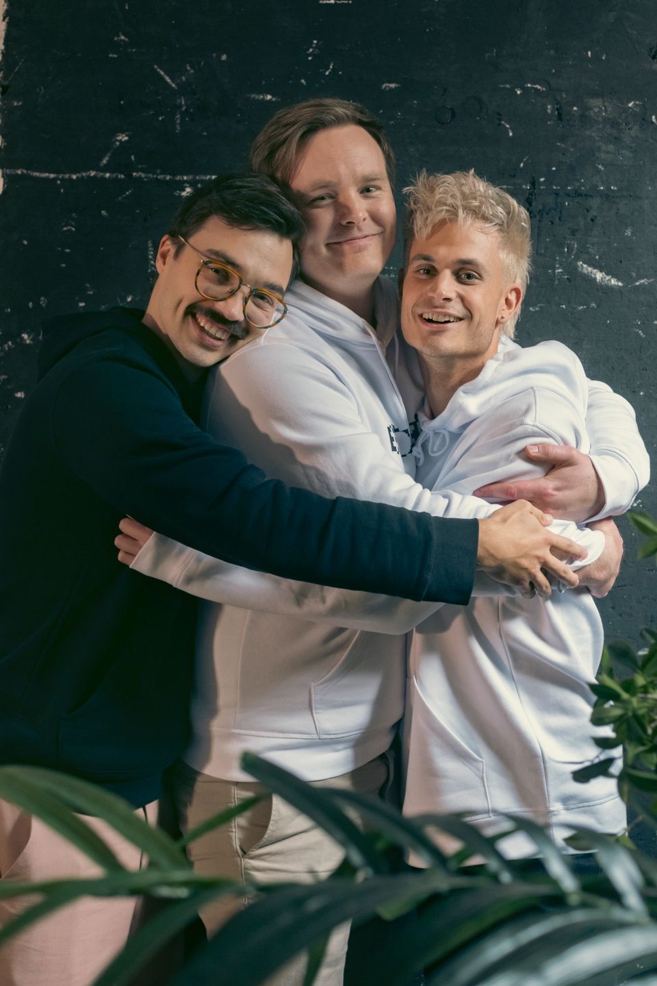 Tre menn med college-gensere står og holder rundt hverandre og smiler mot fotografen.