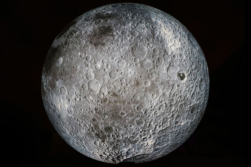 Et nærbilde av Månen viser en grå overflate med mange runde hull og mindre og større kratere i.