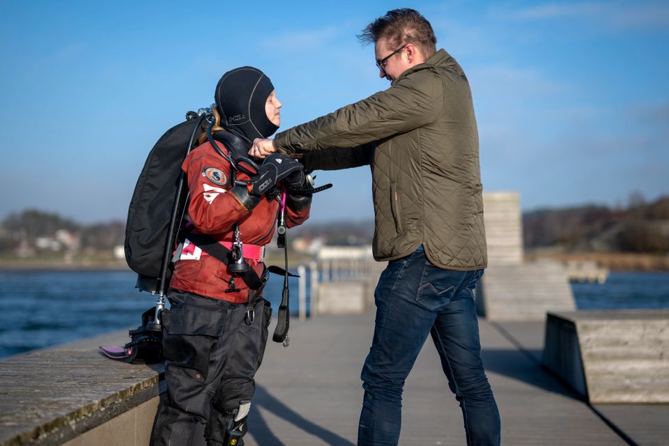 En voksen mann hjelper en jente med å ta på dykkerutstyret.
