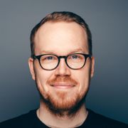 Nærbilde av en mann med briller og rødbrunt hår og skjegg som smiler. 