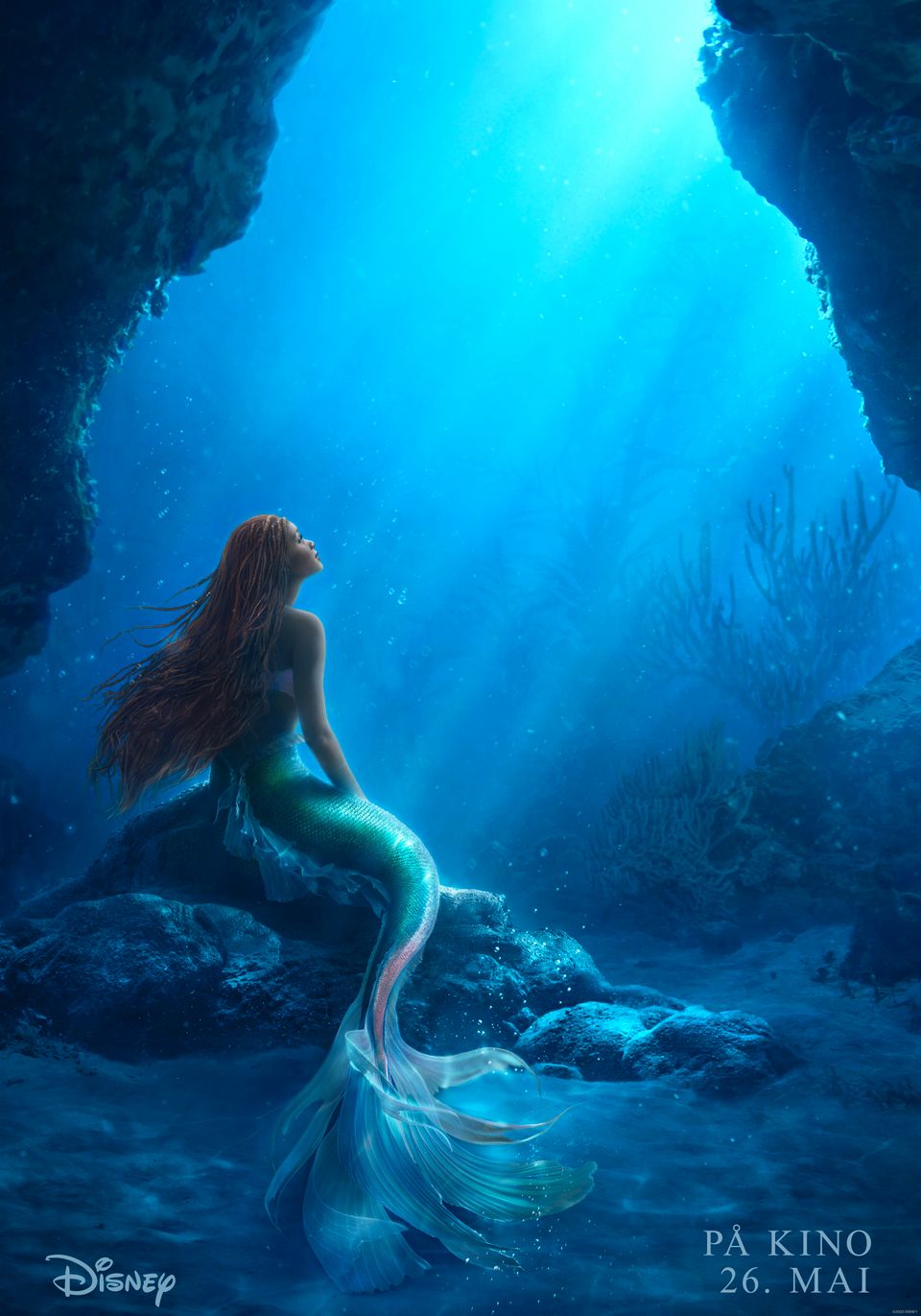 Bilde fra en film som er på havbunnen og det sitter en havfrue med langt rødlig hår som sitter på en stein. 