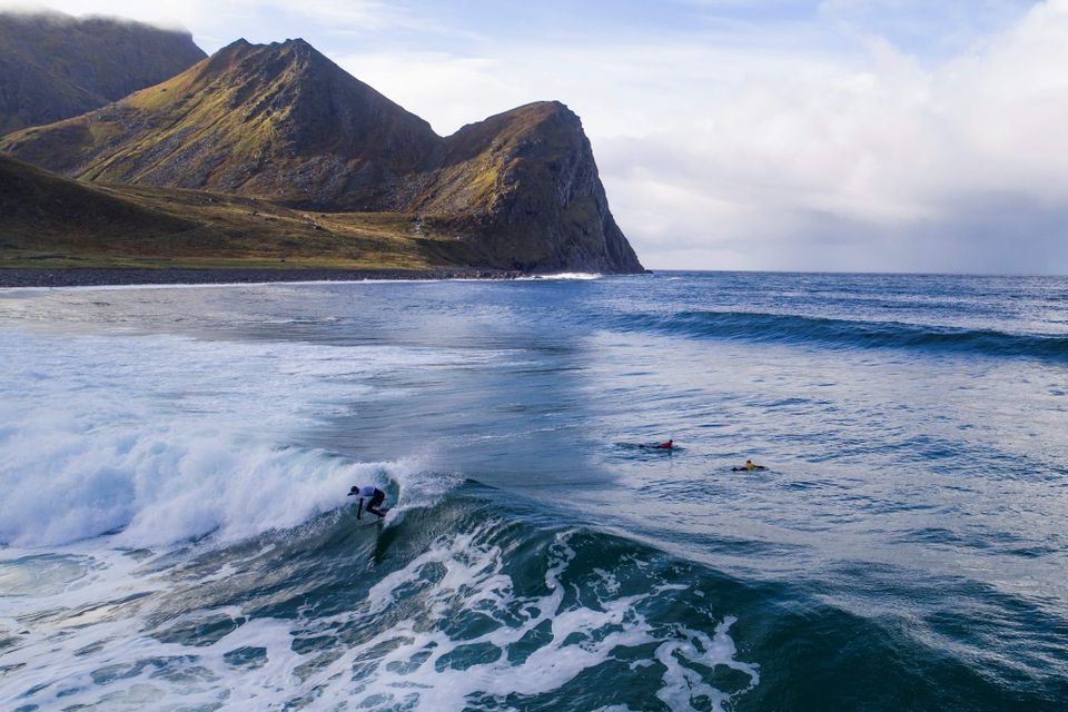 en person surfer på en stor bølge på vannet med et fjell i bakgrunnen. 