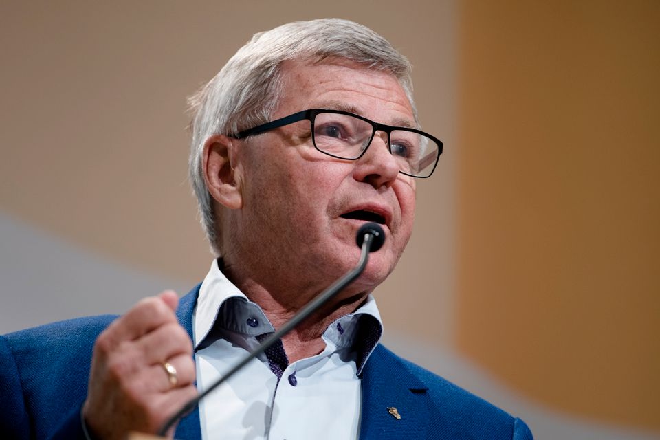 En mann med grått hår og firkantede briller knytter neven mens han snakker i en svart mikrofon.