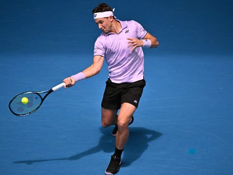 En ung mann med rosa t-skjorte svinger tennis-racketen sin etter en ball på en blå bane.