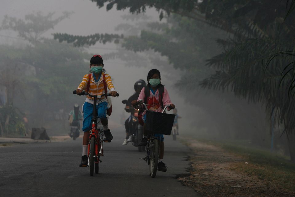 To jenter med munnbind sykler til skolen i forurenset luft.