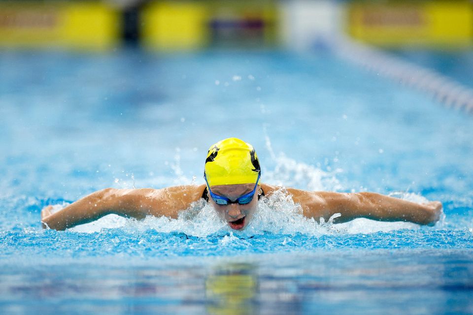 En svømmer med gul hette og svømmebriller er i vannet med armene til siden.