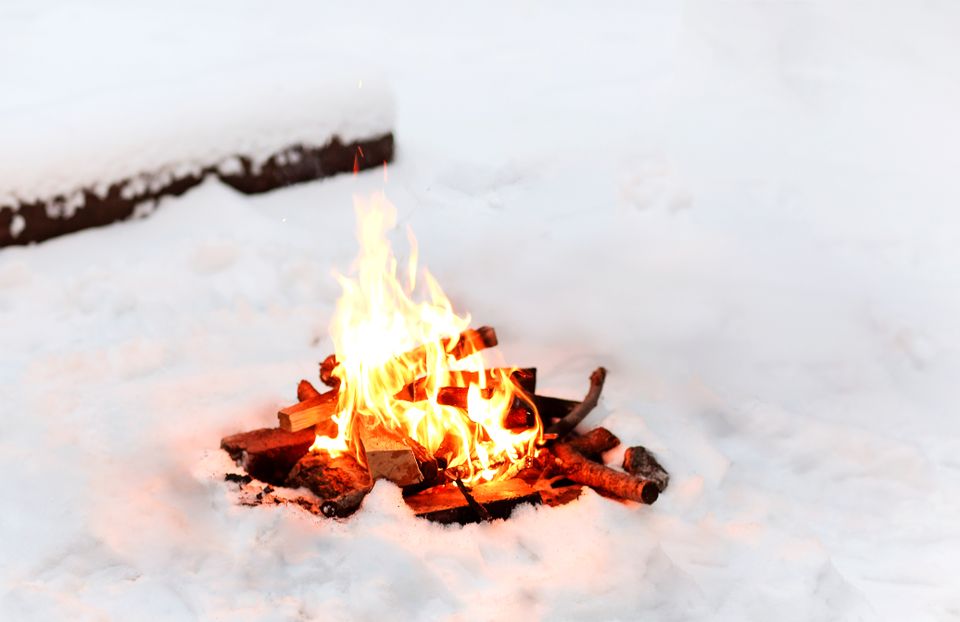 Et bål med røde glør og lysegule flammer brenner i hvit snø.