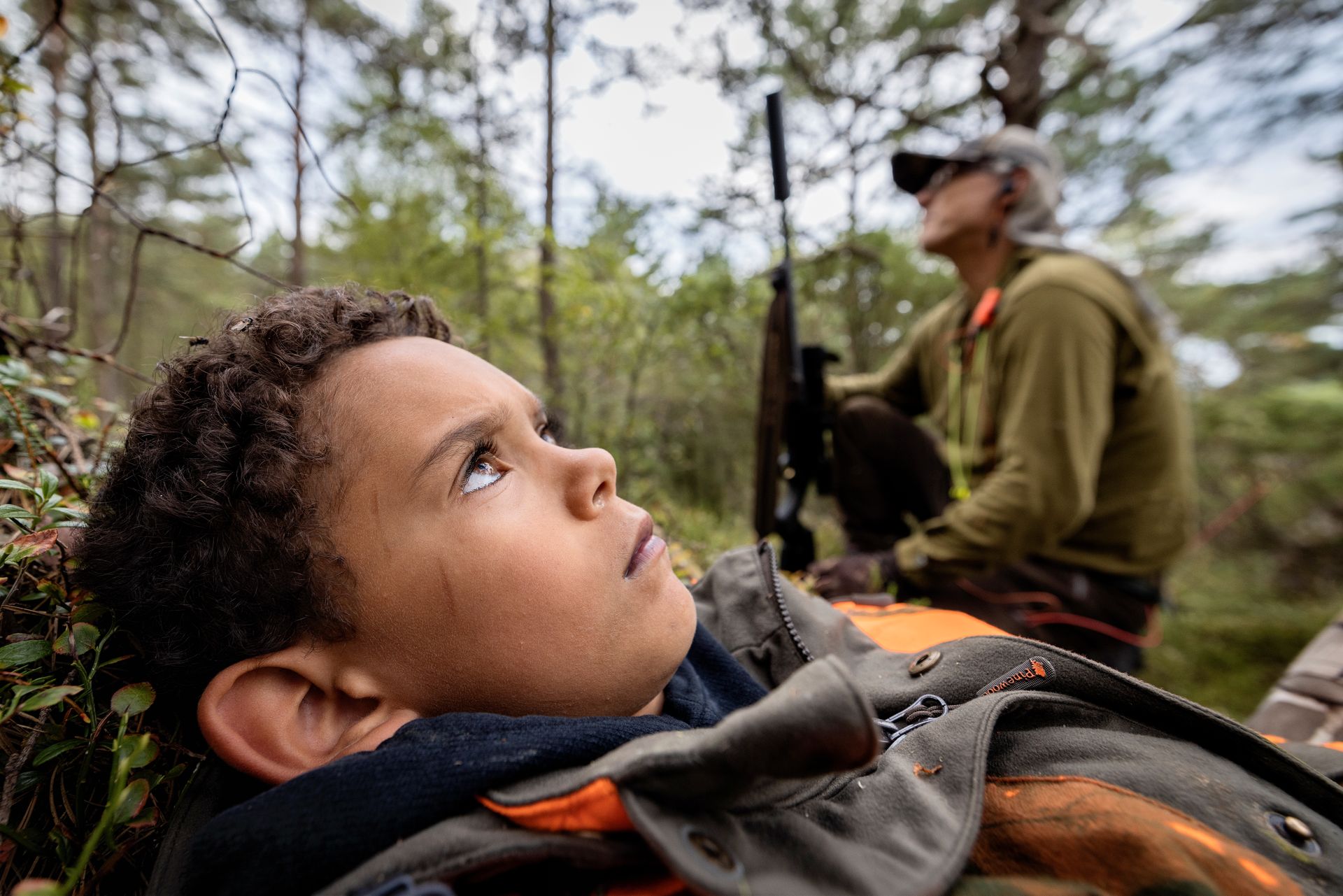 En gutt med mørkt krøllete hår ligger i skogen ved siden av farfaren sin og kikket opp på himmelen. 