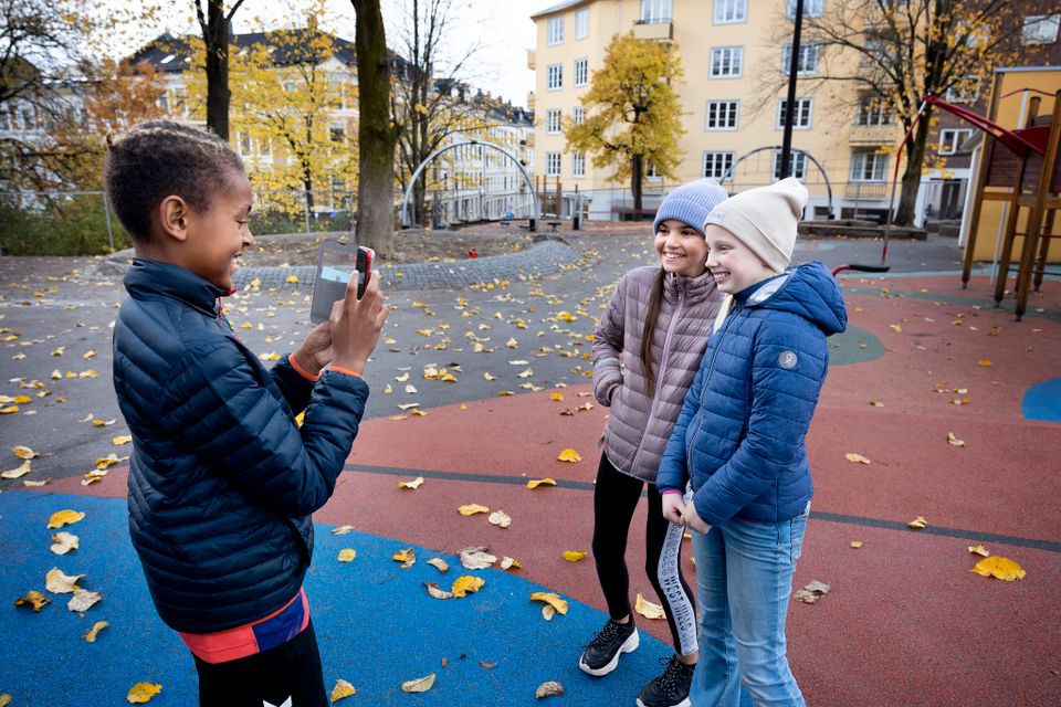 En gutt tar et bilde av to smilende jenter med mobiltelefonen sin.