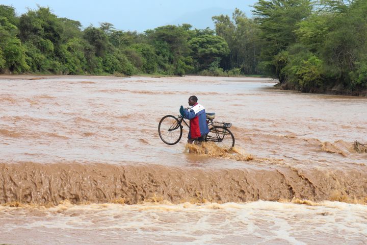 En mann holder i en sykkel mens han forsøker å krysse over en elv.