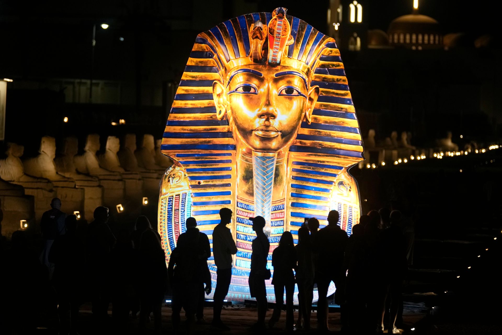 Mange mennesker står i mørket og ser på en enorm egyptisk gull-statue av en ung mann med et stort, blåstripete hodeplagg. 