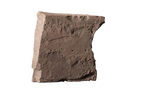 En stor, brun sten med noen innrissede runer, eller bokstaver, er fotografert mot hvit bakgrunn.