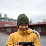 En gutt med gul boblejakke som står ute i en skolegård og ser ned i en smarttelefon. 