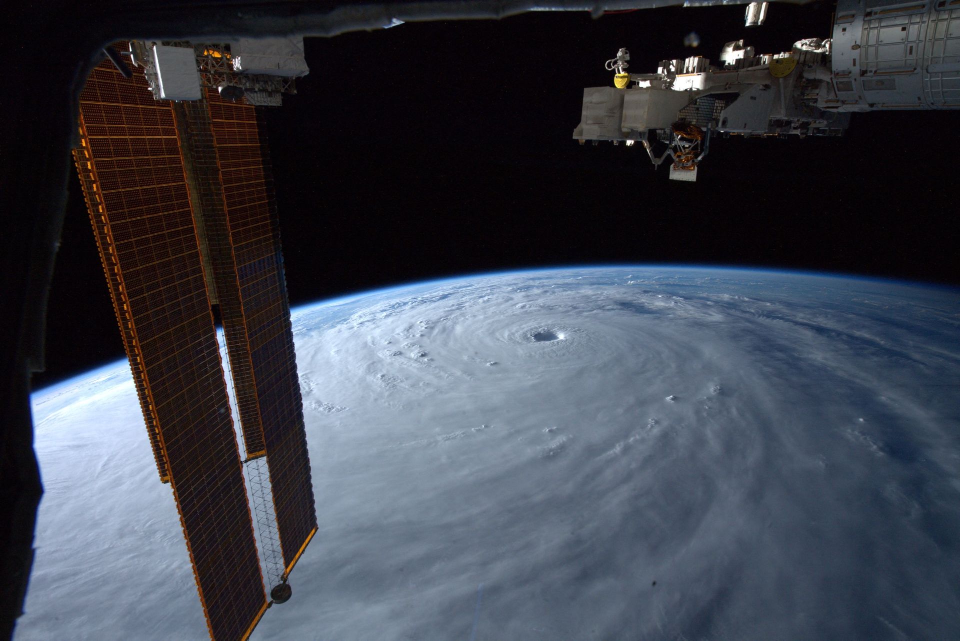 Et bilde tatt fra en satellitt eller en form for romfartøy viser den buede overflaten av Jorden, som er dekket av tykke, hvite skyer som samler seg i en spiral, og i øyet (midten) av stormen er det et slags hull. 