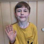 En gutt med pannelugg og gul genser vinker