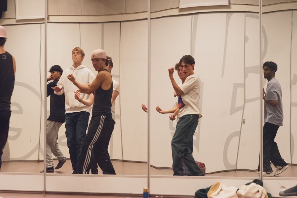 Et bilde som er tatt inn i en speilvegg hvor man ser flere unge menn som øver på å danse. 
