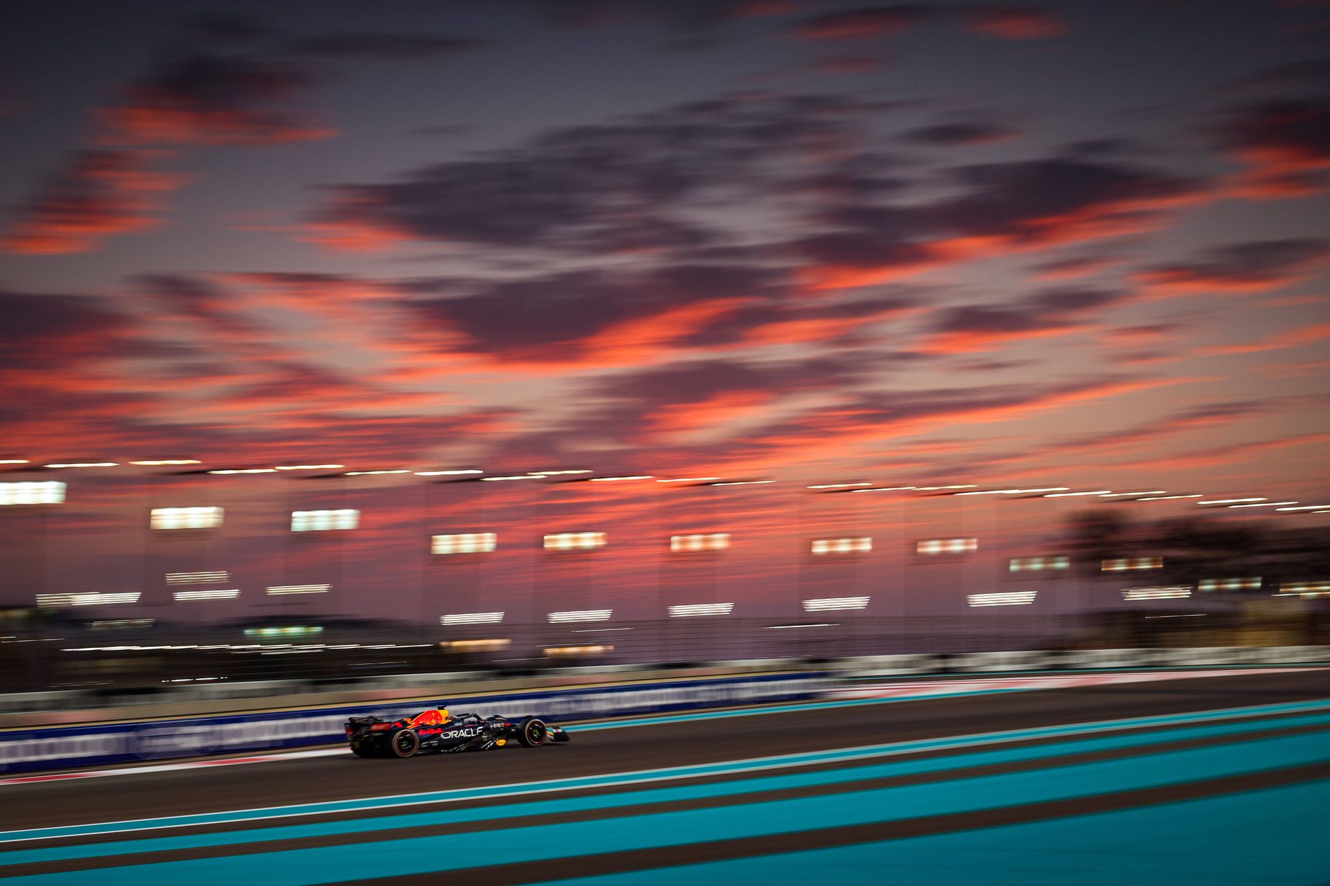 En racerbil med Red Bull-logo på kjører forbi fotografen mens det er en rød solnedgang i bakgrunnen. 