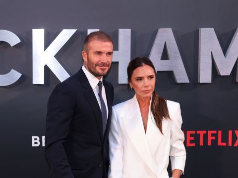 David og Victoria Beckham, i mørk og lys dress, står foran en pressevegg der det står "BECKHAM" og "Netflix".