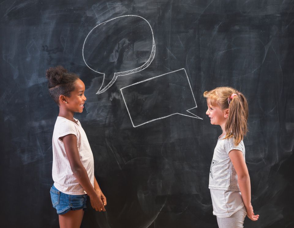 Illustrasjonsbilde av to unge barn som står overfor hverandre, foran en svart tavle, med hver sin tomme snakkeboble tegnet på tavlen. 