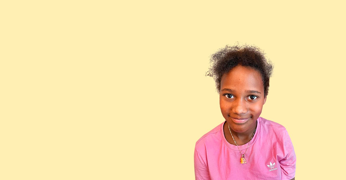 En jente med gul genser og krøllete, mørkebrunt hår smiler forsiktig mot fotografen fra en redigert, gul bakgrunn.