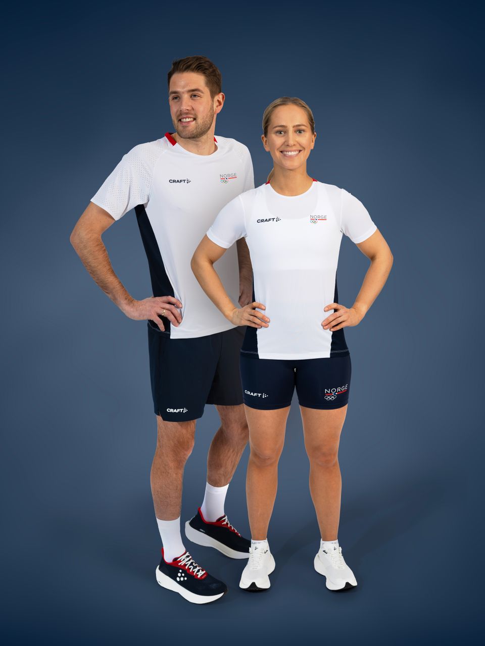 Et bilde av en mann og en dame kledd i hvite t-skjorter og blå shortser, som står med hendene på hoftene og smiler.