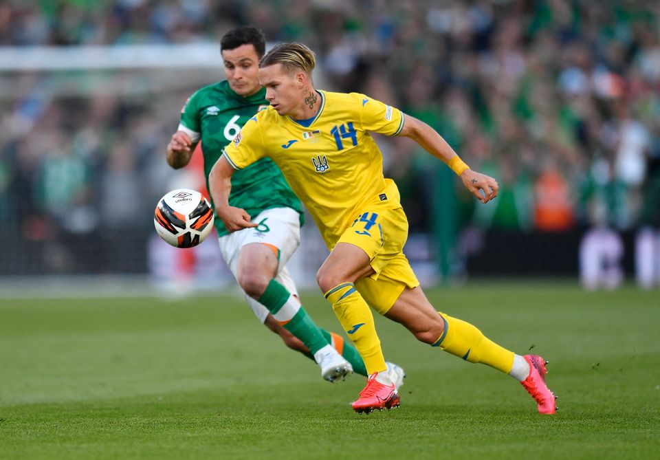 En fotballspiller i gul drakt løper mot en ball med en spiller i grønn og hvit drakt like etter seg. 
