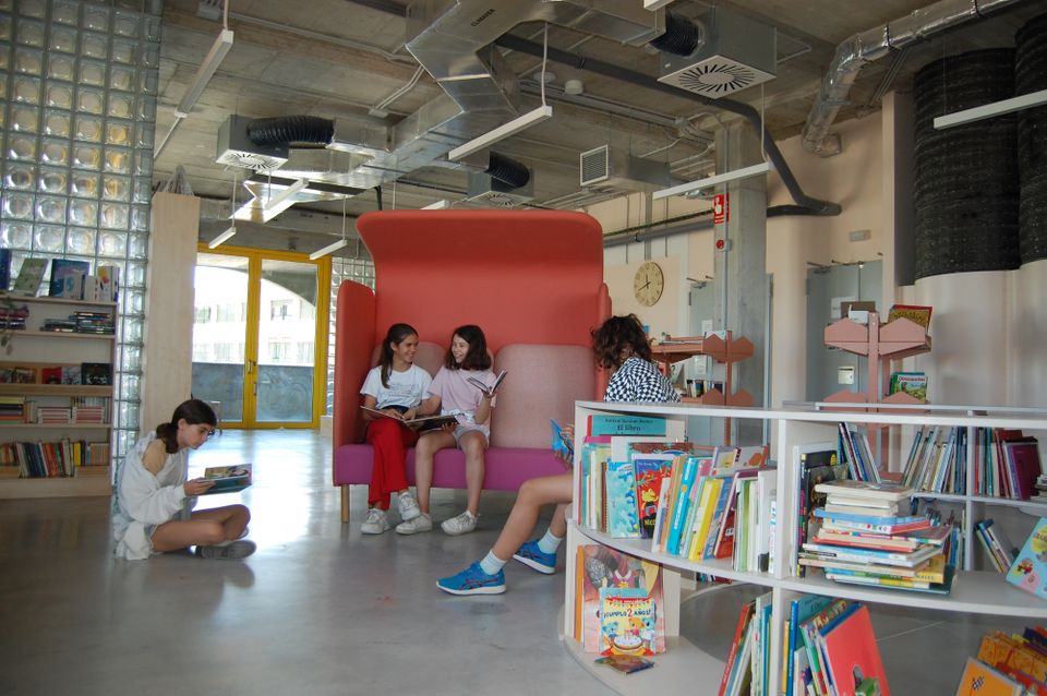 Fire jenter i et skolebibliotek med betong og glassvegger