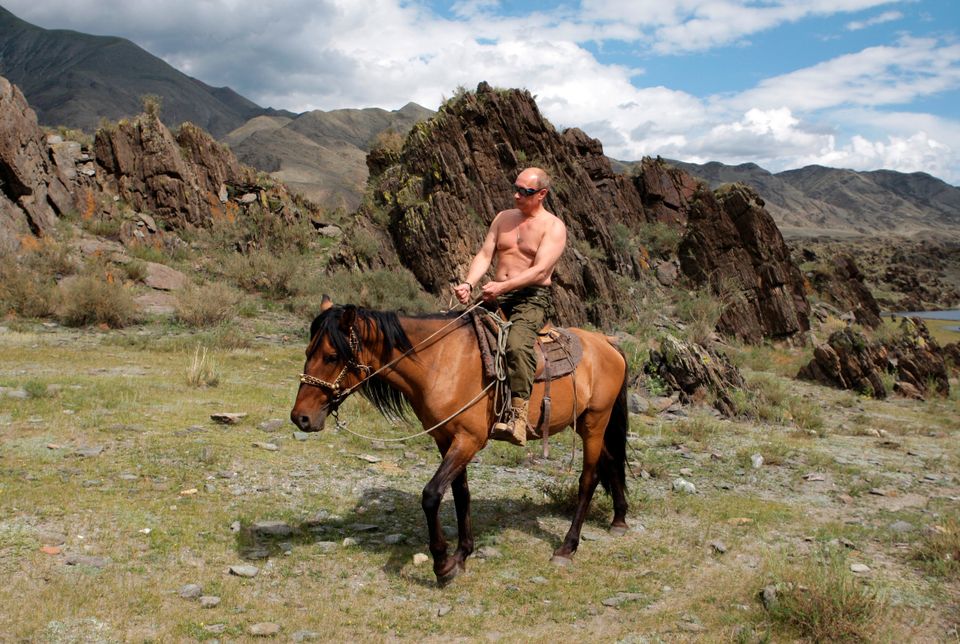 En mann med solbriller og uten klær på overkroppen sitter på en hest.