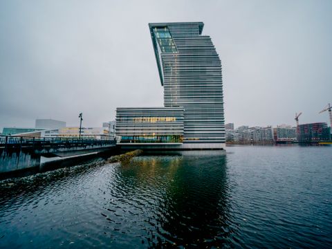 Landskapsbilde av et nytt, høy bygg med skjev topp i sjøkanten i Oslo, av stål og glass. 